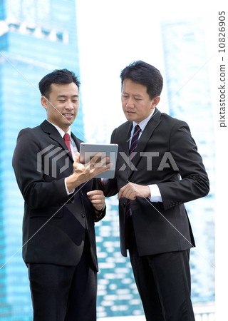 Two successful business men standing in front of glass building using mobile device tablet iPad Two successful business men standing in front of glass building using mobile device tablet iPad 10826905