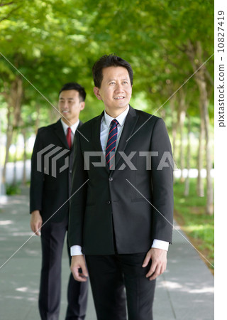 Two successful entrepreneur business men stand front and back along promenade 10827419