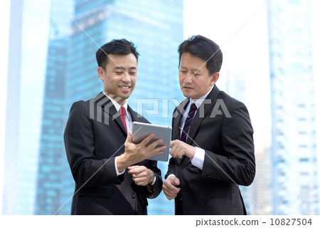 Two successful business men standing in front of glass building using mobile device tablet iPad Two successful business men standing in front of glass building using mobile device tablet iPad 10827504