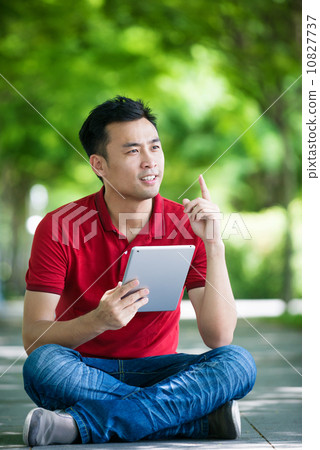 Young man in causal having an idea using iPad mobile device tablet seating along promenade Young man in causal having an idea using iPad mobile device tablet seating along promenade 10827737