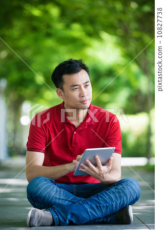 Young man in causal having an idea using iPad mobile device tablet seating along promenade Young man in causal having an idea using iPad mobile device tablet seating along promenade 10827738