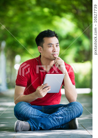 Young man in causal having an idea using iPad mobile device tablet seating along promenade Young man in causal having an idea using iPad mobile device tablet seating along promenade 10827739