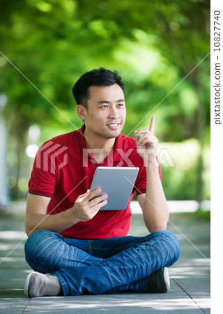 Young man in causal having an idea using iPad mobile device tablet seating along promenade  10827740