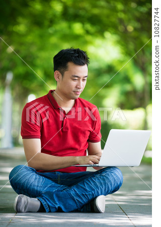 Young man in causal using mobile device laptop seating along promenade Young man in causal using mobile device laptop seating along promenade 10827744