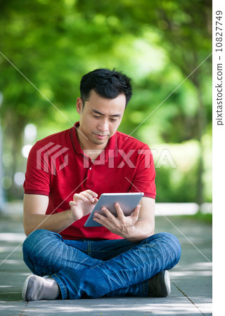 Young man in causal having an idea using iPad mobile device tablet seating along promenade  10827749
