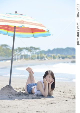 A young lady lying under a beach umbrella and sticking a cheek 10870487