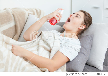 Sick woman lying in living room and using throat spray 10930407