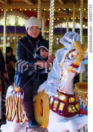 Parent and child riding a merry-go-round 10987733