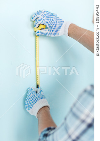 closeup of male in gloves measuring wall with tape 10995443
