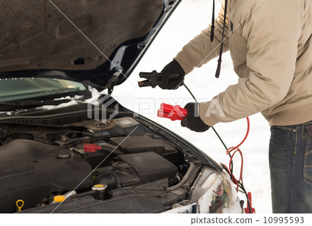 closeup of man under bonnet with starter cables 10995593