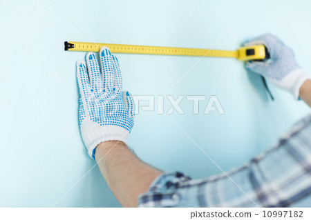 closeup of male in gloves measuring wall with tape 10997182