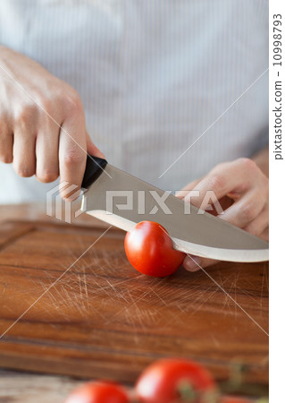 male hand cutting tomato on board with knife 10998793