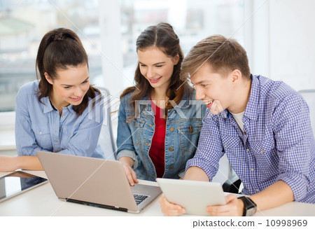 three smiling students with laptop and tablet pc 10998969