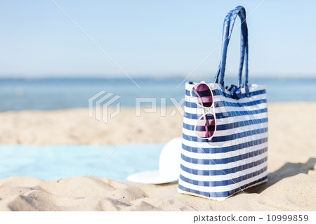 straw hat, sunglasses and bag lying in the sand straw hat, sunglasses and bag lying in the sand 10999859