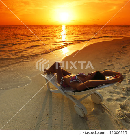 Woman in chaise-lounge relaxing on beach 11006315