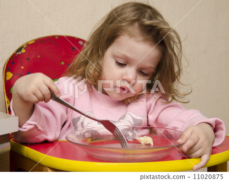 Two-year-old girl eats with a fork at table in kitchen 11020875