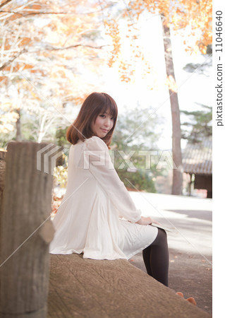 A woman sitting on a park bench that autumn leaves turned A woman sitting on a park bench that autumn leaves turned 11046640
