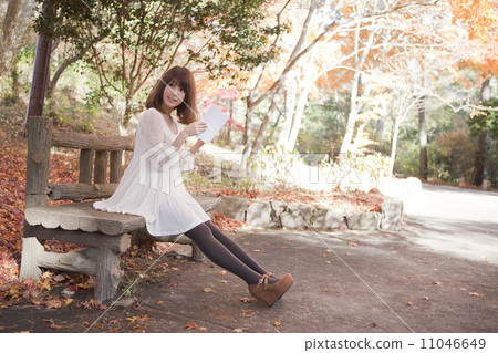 A woman reading with a bench in a park that autumn leaves turned A woman reading with a bench in a park that autumn leaves turned 11046649