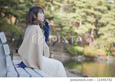 A woman who calls on the bench in front of the pond in the autumn leaves park 11046782