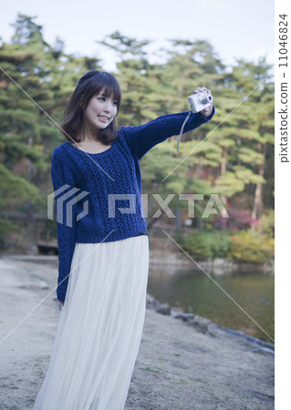 A smiling woman taking a picture in front of a pond in the autumn leaves park A smiling woman taking a picture in front of a pond in the autumn leaves park 11046824