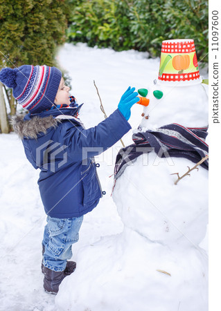 Adorable toddler boy having fun with snowman on winter day Adorable toddler boy having fun with snowman on winter day 11097600