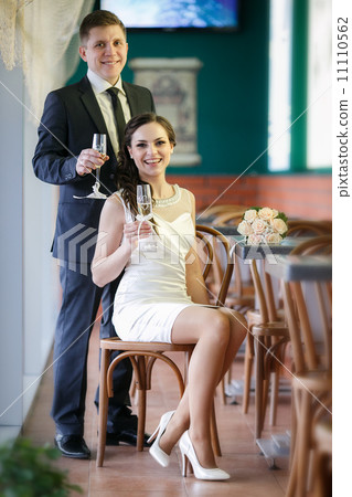 groom with a glass of champagne and the bride with a bouquet from roses in cafe groom with a glass of champagne and the bride with a bouquet from roses in cafe 11110562