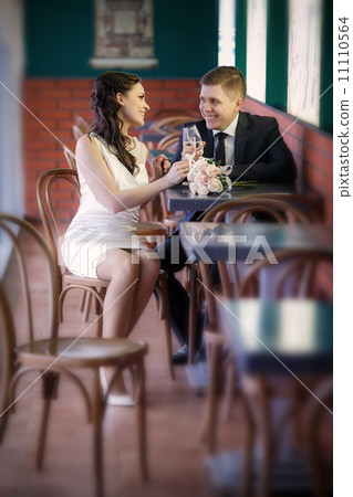 groom with a glass of champagne and the bride with a bouquet from roses in cafe groom with a glass of champagne and the bride with a bouquet from roses in cafe 11110564