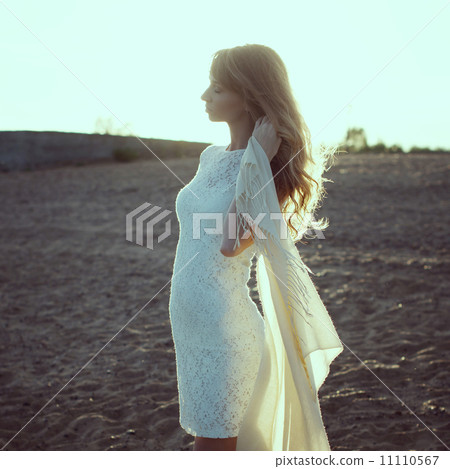 Young woman on beach under sunset light with closed eyes, outdoors portrait. Photo toned in warm col 11110567