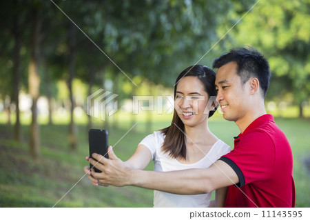 Happy Asian couple in city park using tech. Happy Asian couple in city park using tech. 11143595