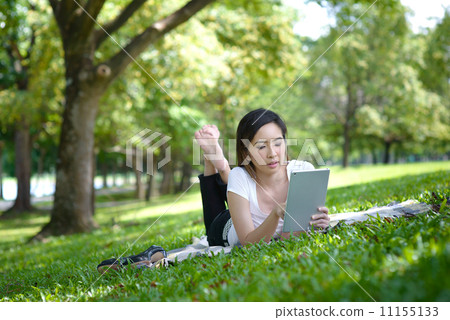 Young woman in a park wearing casual laying on a mat using mobile device tablet iPad 11155133