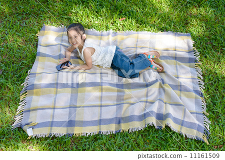Top view of little girl in causal using mobile phone laying on a mat on grass patch  11161509