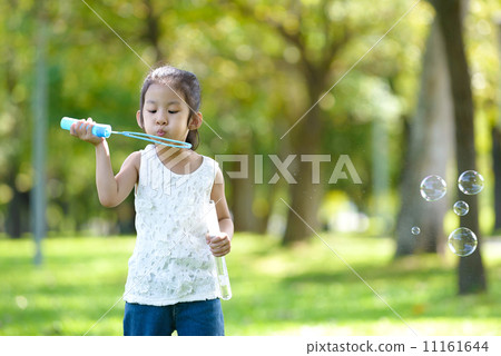 Little girl in causal blowing bubbles in a park Little girl in causal blowing bubbles in a park 11161644