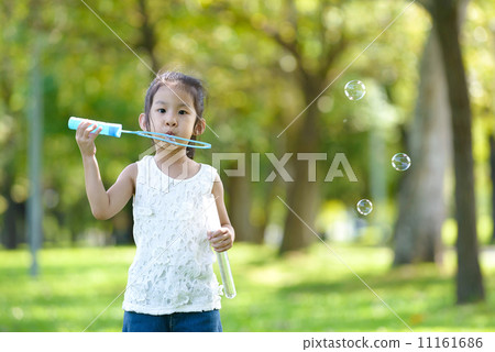 Little girl in causal blowing bubbles in a park 11161686