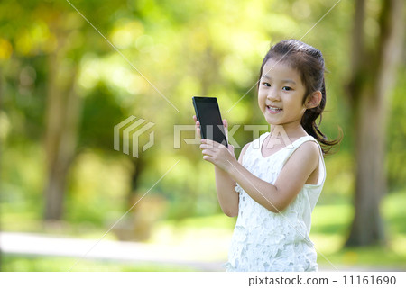 Little girl in causal showing off mobile smart phone in a park 11161690