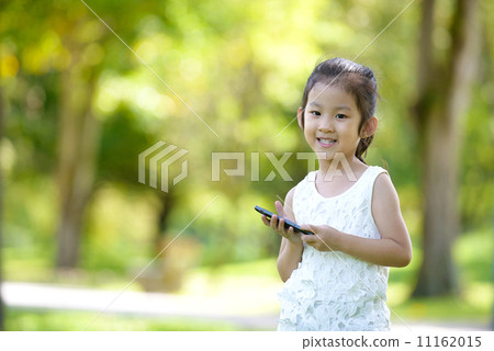 Cute little girl in causal holding mobile smart phone in a park 11162015