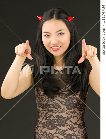 Asian young woman dressed up as an devil pointing towards camera with both hands Asian young woman dressed up as an devil pointing towards camera with both hands 11174434