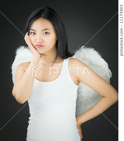 Upset Asian young woman dressed up as an angel with her hands on cheek and hand on hip 11174803