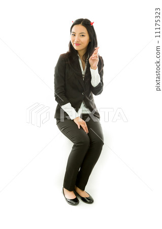 Asian young businesswoman sitting on stool in devil horns with her fingers crossed looking at camera isolated on white background 11175323