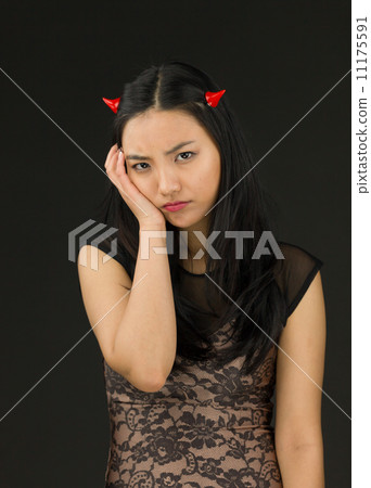 Upset Asian young woman dressed up as an devil with her hand on cheek 11175591