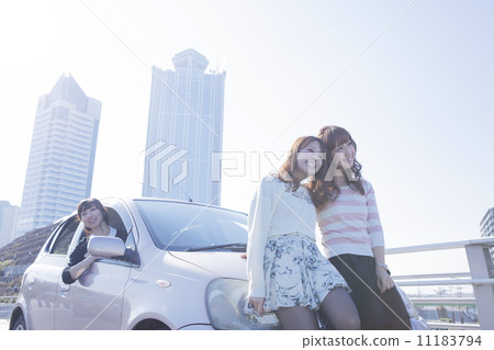 A woman who takes a face from the driver's seat and a friend who cuddles closely in front of the car 11183794