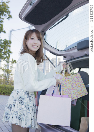 A woman carrying a shopping bag on the trunk of a car 11183795
