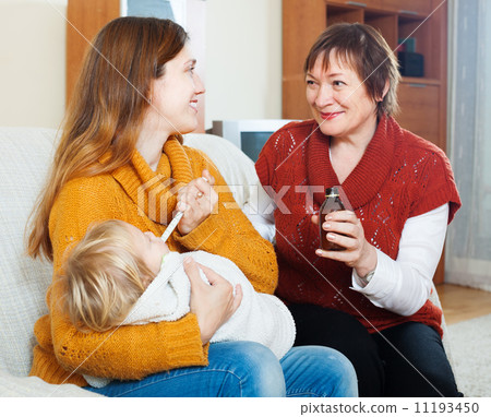 woman with mature mother giving syrup to unwell baby woman with mature mother giving syrup to unwell baby 11193450