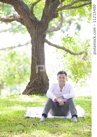 Young man in causal relaxing sitting on a mat in a park 11213480