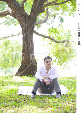 Young man in causal looking troubled sitting on a mat in a park Young man in causal looking troubled sitting on a mat in a park 11213485