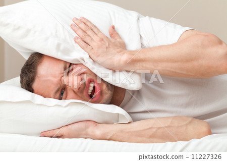 Portrait of Young Caucasian man in bed angry about noise Portrait of Young Caucasian man in bed angry about noise 11227326