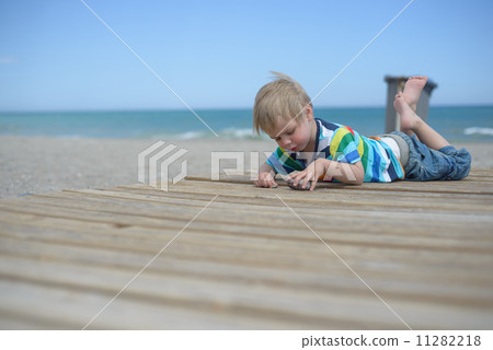 Boy resting on a wooden walkway on the beach Boy resting on a wooden walkway on the beach 11282218