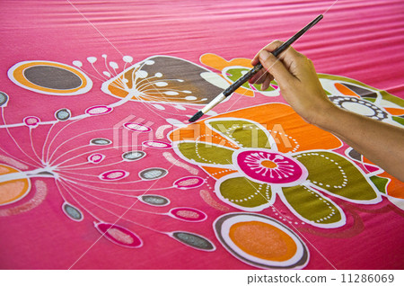 An artist carefully paint the floral/flower motif on a red silk batik fabric 11286069