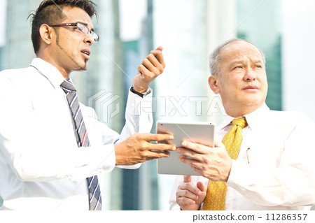 Young executive presenting to senior executive using tablet & pointing to a direction 11286357