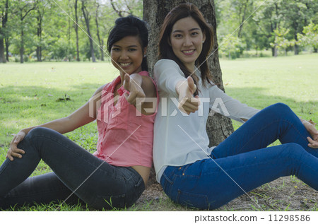 Two Girls Sitting Under a Tree in a park 11298586