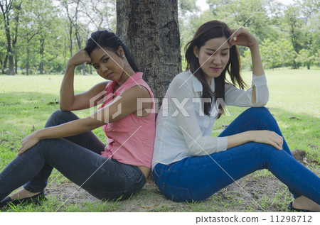 Two Girls Sitting Under a Tree in a park 11298712